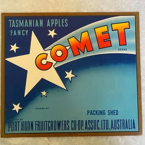 Puede incluir: Una etiqueta vintage para manzanas de Tasmania, con un fondo azul, una estrella blanca y un cometa rojo, naranja y amarillo con la palabra "COMET" en contorno blanco. La etiqueta también incluye el texto "TASMANIAN APPLES FANCY" y "PACKED BY PORT HUON FRUITGROWERS CO-OP. ASSOC.LTD. AUSTRALIA".