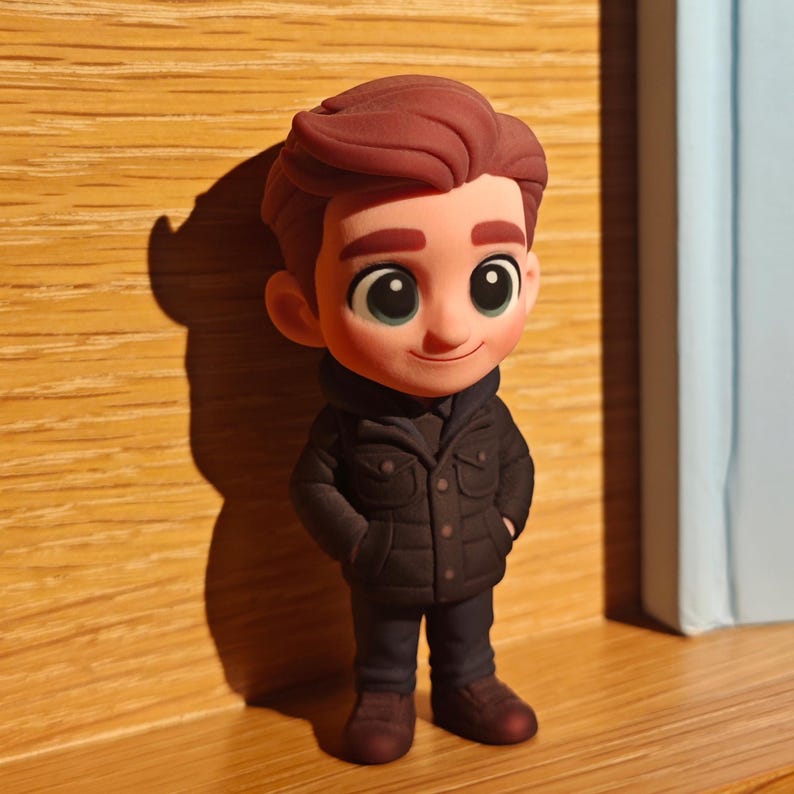 Op de afbeelding: Een cartoonfiguur met bruin haar, gekleed in een donkerbruine jas, een donkerblauwe broek en bruine schoenen. Het personage heeft grote groene ogen en glimlacht. Het beeldje staat op een houten oppervlak.