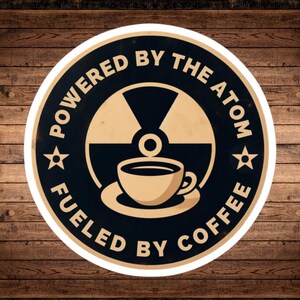 May include: A white circle sticker with black text that reads "Powered by the Atom Fueled by Coffee". Inside the circle is a black and white stylized image of a nuclear symbol with a coffee cup in the center.