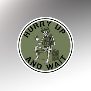 May include: A round sticker featuring a skeleton in military gear, holding a pocket watch. The skeleton is seated on a box, with the words "HURRY UP AND WAIT" encircling the image in black text on a green background.