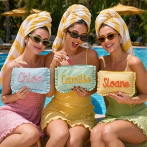 May include: Three rectangular straw pouches with ruffled edges, each featuring a name embroidered in cursive script: Chloe in pink on a light blue pouch, Camilla in yellow on a mint green pouch, and Sloane in orange on a yellow pouch.