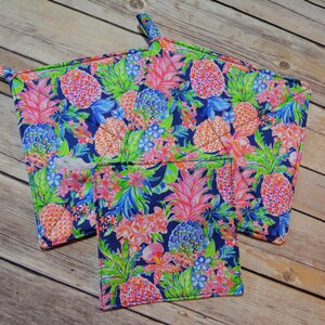May include: Set of three blue and white pot holders with a pineapple print. The largest pot holder has a loop handle.
