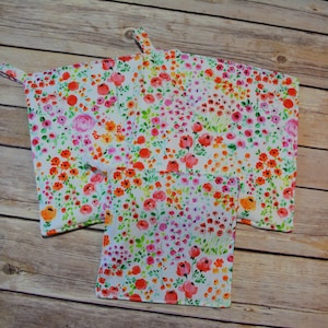 May include: A white floral print oven mitt and matching potholder set. The pattern features a watercolor design of pink, orange, and red flowers with green leaves. The oven mitt has a loop for hanging.