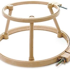 May include: A beige plastic embroidery hoop stand with a circular base and three legs. The hoop is adjustable and has a screw to tighten it.
