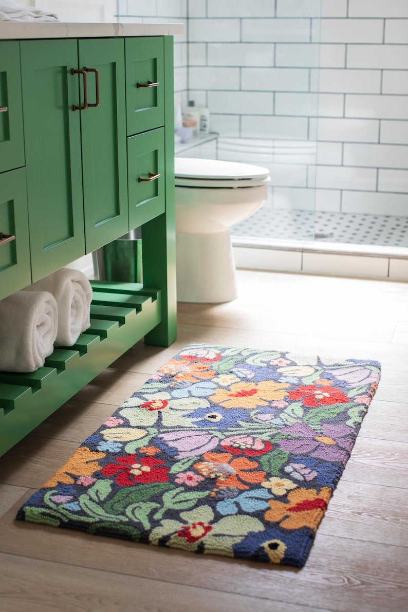 May include: A rectangular floral bath mat with a dark blue background and colorful flowers in red, orange, purple, and yellow. The mat is placed on a light wood floor in a bathroom setting.