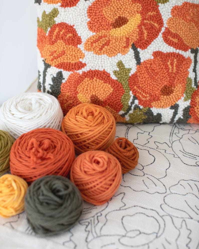 May include: A close-up of a variety of yarn balls in different colours, including white, orange, and green. The yarn balls are arranged on a white surface with a floral pattern.
