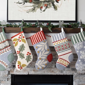 May include: Five textured Christmas stockings hanging in a row, each featuring unique patterns including snowflakes, holly leaves, berries, and geometric stripes in shades of cream, sage green, slate blue, and red, crafted with a looped yarn finish.