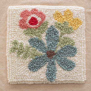 May include: A hand-stitched rug with a floral design. The rug features a large blue flower with a brown center, surrounded by smaller pink and yellow flowers.