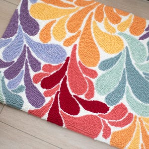 May include: A colorful rug with a white background and a pattern of abstract shapes in shades of purple, blue, green, red, orange, and yellow.