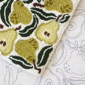May include: A close-up of a handmade rug with a pear design. The rug features green and yellow pears with dark green leaves and brown stems on a white background. The design is repeated on the canvas.