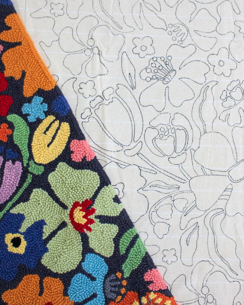 May include: A colorful, floral-patterned rug with a dark blue background. The rug features a variety of flowers in shades of orange, red, blue, green, and pink. Next to the rug is a white fabric with a floral outline design.