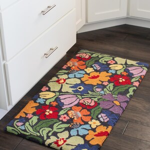 May include: A rectangular floral rug with a dark background and a vibrant array of flowers in red, orange, yellow, blue, and purple. The rug is placed on a dark wood floor near white cabinets.