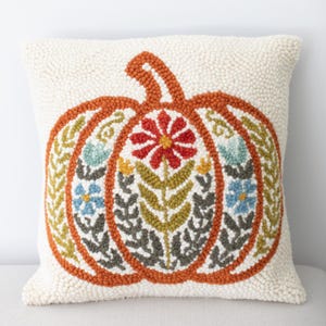 May include: Cream-colored decorative pillow with a large orange pumpkin design. The pumpkin is filled with floral and leaf patterns in red, green, blue, and yellow. The pillow has a textured, tufted appearance.
