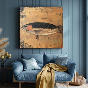 May include: A large, rectangular painting of a fish with a black back and orange eye hangs on a blue wall. The fish is painted on a gold-toned background. A blue sofa with pillows and a yellow blanket are in front of the wall.