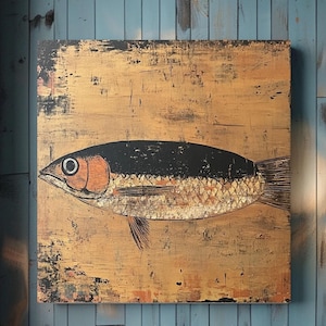 May include: A square wall art piece featuring a stylized fish illustration centered on a textured, metallic gold background. The fish has a black upper body, a copper-toned head, and a gold-leaf style scale pattern, with dark distressed edges.