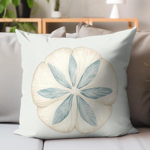 May include: A decorative throw pillow with a watercolor design. The pillow features a large, stylized flower in shades of cream and light blue. The flower's petals are arranged in a circular pattern, creating a symmetrical design. The pillow is on a light gray background.