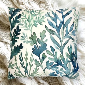 May include: Square cushion featuring a watercolour design of blue and green leafy plants on a cream background. The cushion showcases a variety of leaf shapes and sizes, creating a natural aesthetic. Ideal for adding a touch of nature to any room.