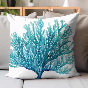 May include: A white square throw pillow featuring a watercolor design of a blue coral reef. The coral is a vibrant mix of turquoise and teal, creating a striking contrast against the white background. The pillow is placed on a gray sofa.