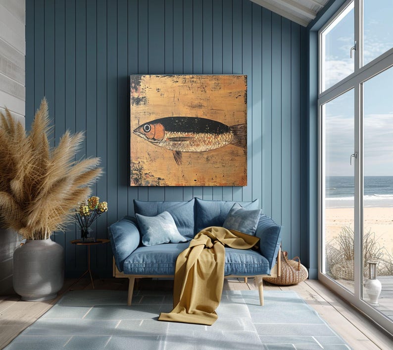 May include: A large, rectangular painting of a fish with a black back and orange eye hangs on a blue wall. The fish is painted on a gold-toned background. A blue sofa with pillows and a yellow blanket are in front of the wall.