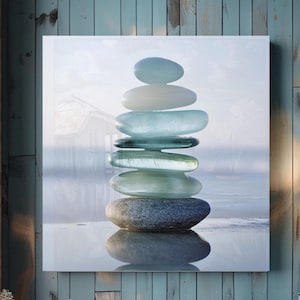 May include: A square wall art print featuring a vertical stack of seven smooth, rounded stones. The bottom stone is dark gray, while the six stones above it are translucent, varying in shades of pale blue, seafoam green, and white.