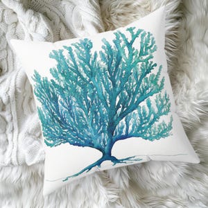 May include: White square throw pillow featuring a watercolor design of a teal coral reef. The coral is detailed with varying shades of teal and blue. The pillow is on a white, textured surface.