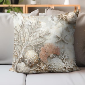 以下が含まれることがあります： 海岸をテーマにした正方形の装飾用クッション。 白、ベージュ、コーラルの色合いのサンゴ、ヒトデ、ウニのテクスチャデザインが、まだら模様の背景に施されています。 クッションは白いソファの上に置かれています。