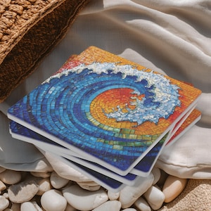May include: A stack of square coasters with a mosaic wave design. The wave features shades of blue, orange, and white, creating a vibrant ocean scene. The coasters are stacked on a bed of white pebbles.