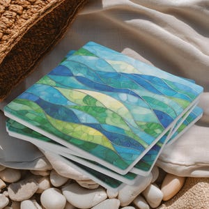 May include: Four square coasters with a blue, green, and yellow wave design. The coasters have a white border and are stacked on a white surface. The coasters are resting on small, smooth stones.