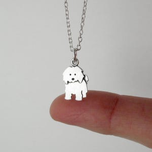 May include: A silver-toned metal necklace featuring a small, flat pendant shaped like a shaggy dog. The pendant is suspended from a delicate silver-toned chain link necklace. The dog charm has simple cut-out details for eyes and a nose.
