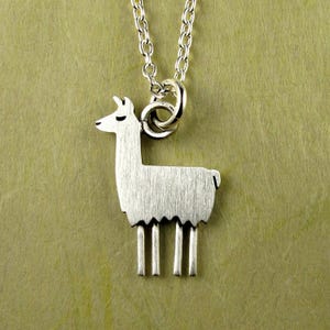 May include: A silver-colored llama pendant necklace. The llama charm is detailed with a textured surface and four legs. The necklace chain is also silver and hangs from a circular bail.