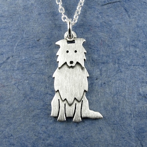 Op de afbeelding: Een zilverkleurige hangerketting met een gestileerd honden silhouet. De hanger toont een zittende hond met een getextureerd oppervlak, hangend aan een fijne zilveren ketting. De hond heeft een gedetailleerd gezicht en een pluizige vacht.