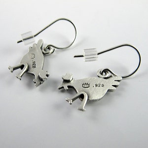 May include: A pair of sterling silver drop earrings shaped like chickens. Each earring features a textured finish, a hook-style wire, and a clear plastic backing. The back of each chicken charm is stamped with a small sun-like icon and the text .925.