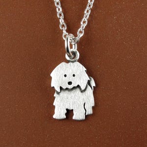 May include: A silver-toned metal pendant shaped like a shaggy dog with a brushed finish, suspended from a matching silver-toned link chain. The dog charm features simple cut-out details for the eyes and nose, creating a distinct silhouette.