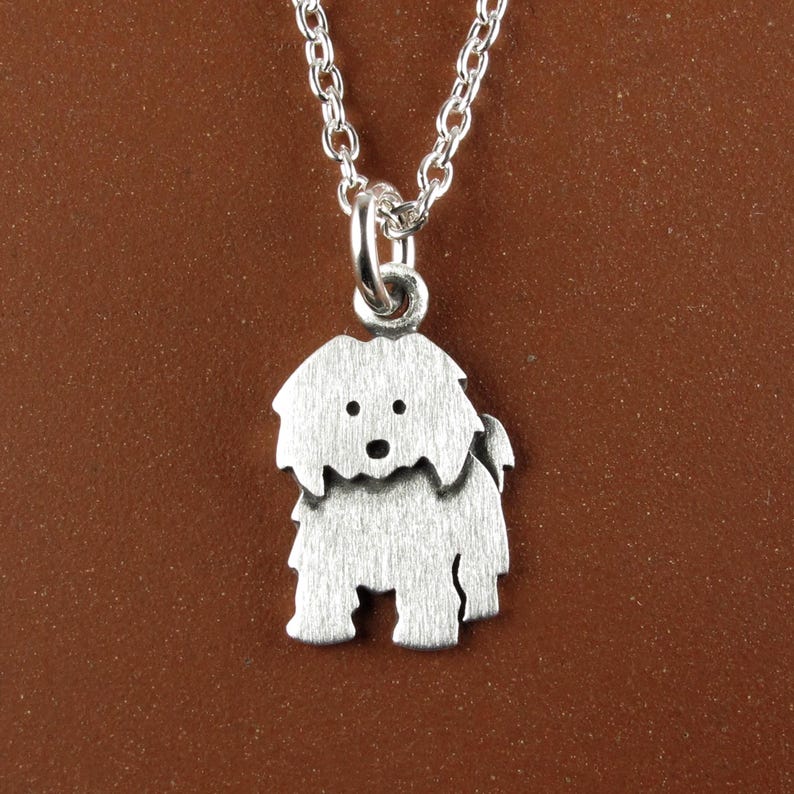 May include: A silver-toned metal pendant shaped like a shaggy dog with a brushed finish, suspended from a matching silver-toned link chain. The dog charm features simple cut-out details for the eyes and nose, creating a distinct silhouette.