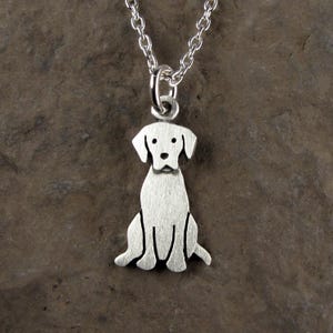 May include: A silver-toned metal pendant shaped like a sitting dog, featuring a brushed finish and simple engraved lines for facial features and body contours. The pendant hangs from a matching silver-toned metal link chain necklace.