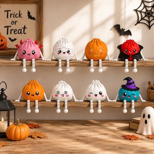 May include: Eight small, round, cartoon-style figurines with dangling legs, each featuring a unique Halloween theme including a pink devil, white mummy, orange pumpkin, red vampire, orange jack-o'-lantern, white ghost, and a teal witch.