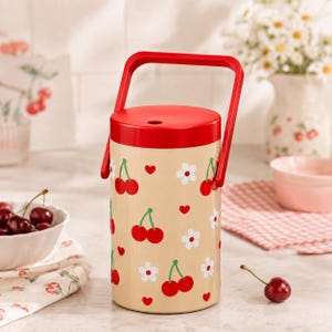 May include: A cylindrical beige container with a bright red lid and a matching red swing handle. The exterior features a repeating pattern of small red cherries, white five-petaled flowers, and tiny red hearts printed across the surface.
