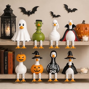 May include: A collection of eight decorative duck figurines dressed in Halloween costumes, including a ghost, Frankenstein, mummy, vampire, pumpkin-headed duck, witch, skeleton, and wizard, all featuring dangling orange feet.