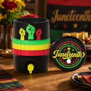 May include: A black beverage dispenser with a yellow, green, and red horizontal band and three raised fist icons in yellow, green, and red. The lid features a circular graphic with the text Juneteenth, Honoring the Past, Celebrating Freedom.