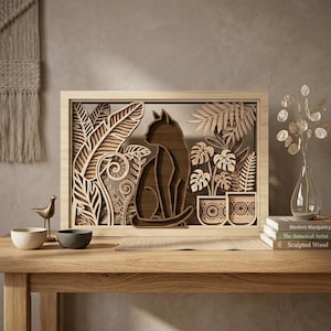 May include: Wooden layered art piece featuring a cat silhouette amidst detailed botanical elements. The artwork, in a natural wood tone, includes plants and potted greenery, all within a rectangular frame. The piece is displayed on a wooden table with decorative items.