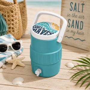 May include: A teal beverage cooler with a white handle and a white lid featuring the text "HAPPINESS COMES IN WAVES" in dark blue and orange. The cooler has a white spigot at the base for dispensing liquid and a textured middle section.