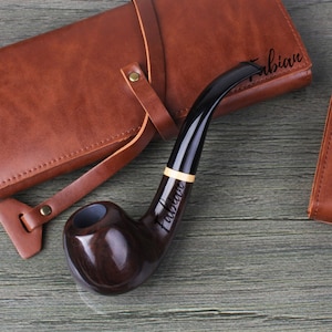 May include: A dark brown wooden pipe with a black stem and a gold band. The pipe is engraved with the name "Fabian".