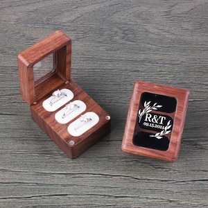 May include: Two wooden ring boxes. One box has three ring slots and a clear lid. The other box has a black velvet interior with an engraved design that says "R&T 09.15.2024".