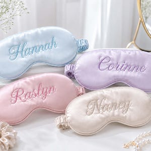 Peut inclure: Quatre masques de sommeil en satin avec bandeaux élastiques en bleu clair, lavande, rose pâle et champagne. Chaque masque présente une broderie personnalisée avec les prénoms Hannah, Corinne, Raslyn et Nancy cousus en écriture cursive.