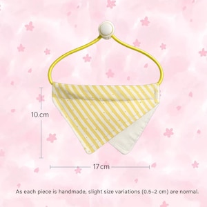 May include: A yellow and white striped bandana, 17 cm wide and 10 cm high, hangs from a yellow hanger. The bandana has a white interior and is handmade. The background is a pink floral pattern.