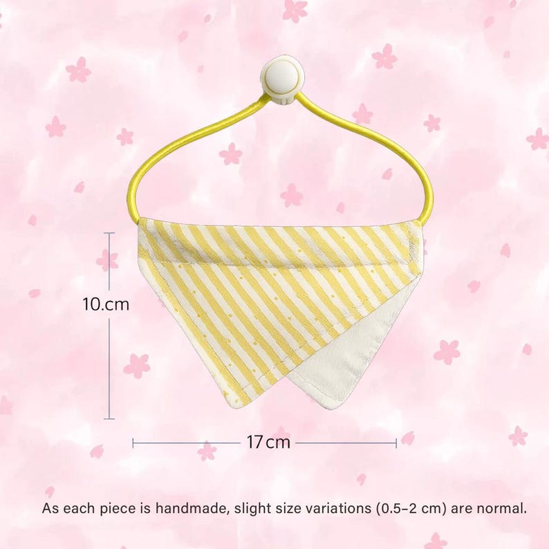 May include: A yellow and white striped bandana, 17 cm wide and 10 cm high, hangs from a yellow hanger. The bandana has a white interior and is handmade. The background is a pink floral pattern.