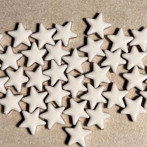 May include: A collection of white ceramic star-shaped tiles. The tiles are arranged in a loose, organic pattern.