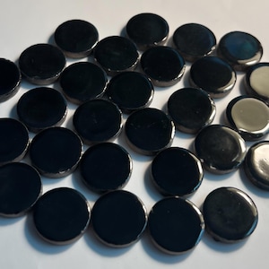 May include: A collection of glossy, black, round glass tiles. Each tile has a slightly raised edge and a reflective surface. The tiles are scattered across a white surface, creating a pattern of dark circles.
