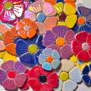 Könnte beinhalten: Nahaufnahme eines Mosaiks aus bunten Keramikblumen in Rot, Blau, Orange, Lila und Gelb. Jede Blume hat eine zentrale Scheibe und blütenblattförmige Fliesen. Die Anordnung zeigt die komplizierten Details und lebendigen Farben.