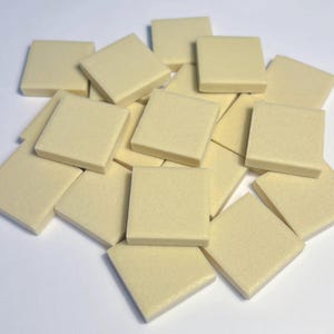 May include: A pile of small, square, cream-coloured tiles. The tiles are arranged in a haphazard manner, with a slightly textured surface. The colour is a pale yellow, and the edges are neat and well-defined. These tiles are likely for a craft or mosaic project.